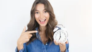 girl with long brown hair holding old fashioned alarm clock to signify time management