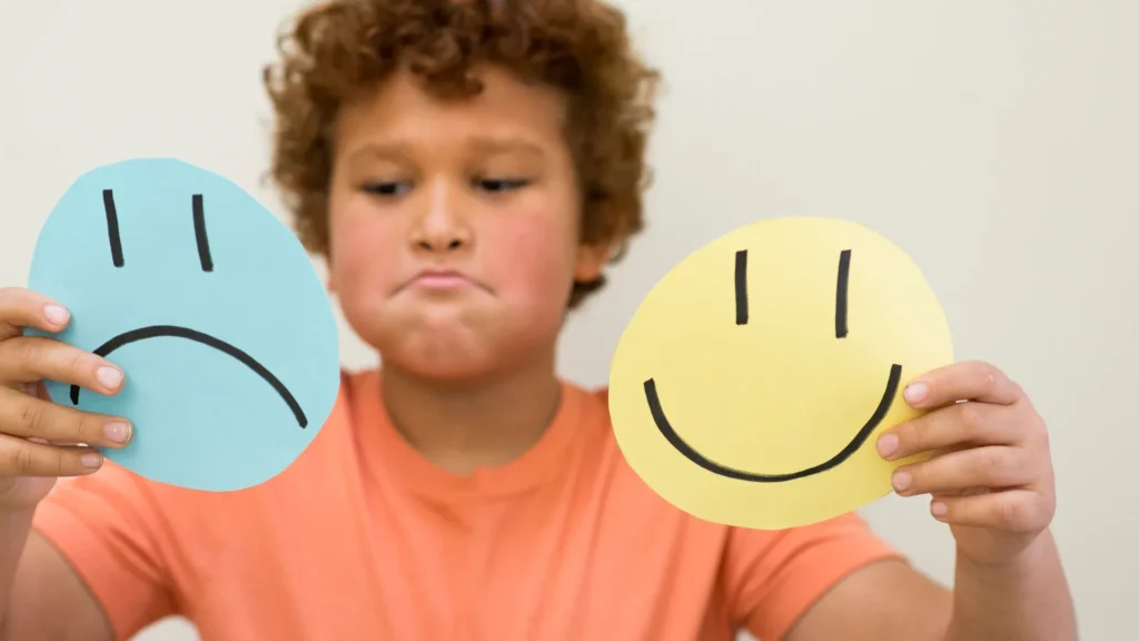 young boy holding up a sad face and a happy face